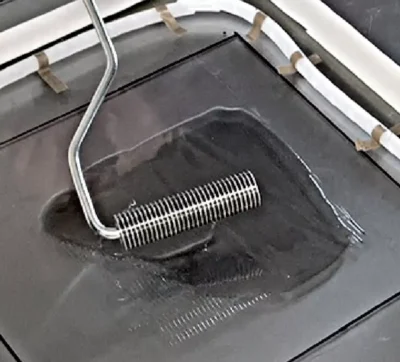 Graphene product depicted in a liquid form on a glass plate, spread using a metal object that distributes the substance equally on a surface.