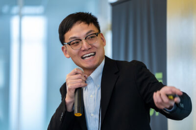 Ray Zu, co-founder of Fermi Energy, holding mic and smiling as he presents the company's materials that produce higher than average performing batteries for electric vehicles.