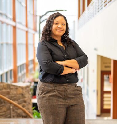 Female staff who oversees the program mentioned in the article, stands in a open light filled lobby with her arms crossed looking at the camera.