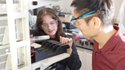 Female and male wearing saftey goggles work in a sodium-ion battery technology lab setting.